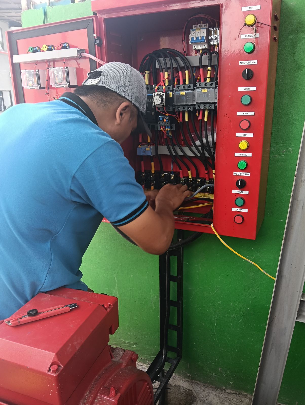 Teknisi maintenance memeriksa panel kontrol pompa hydrant dan sistem kelistrikan gedung